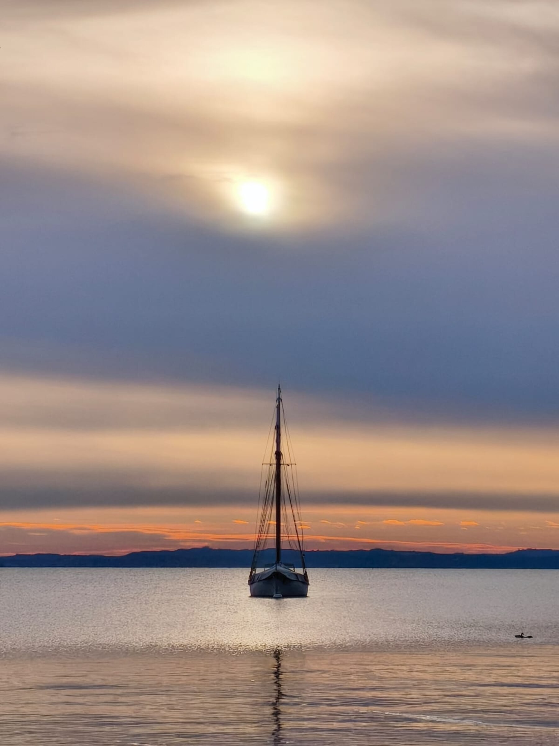 A quiet sailboat on calm water at sunset